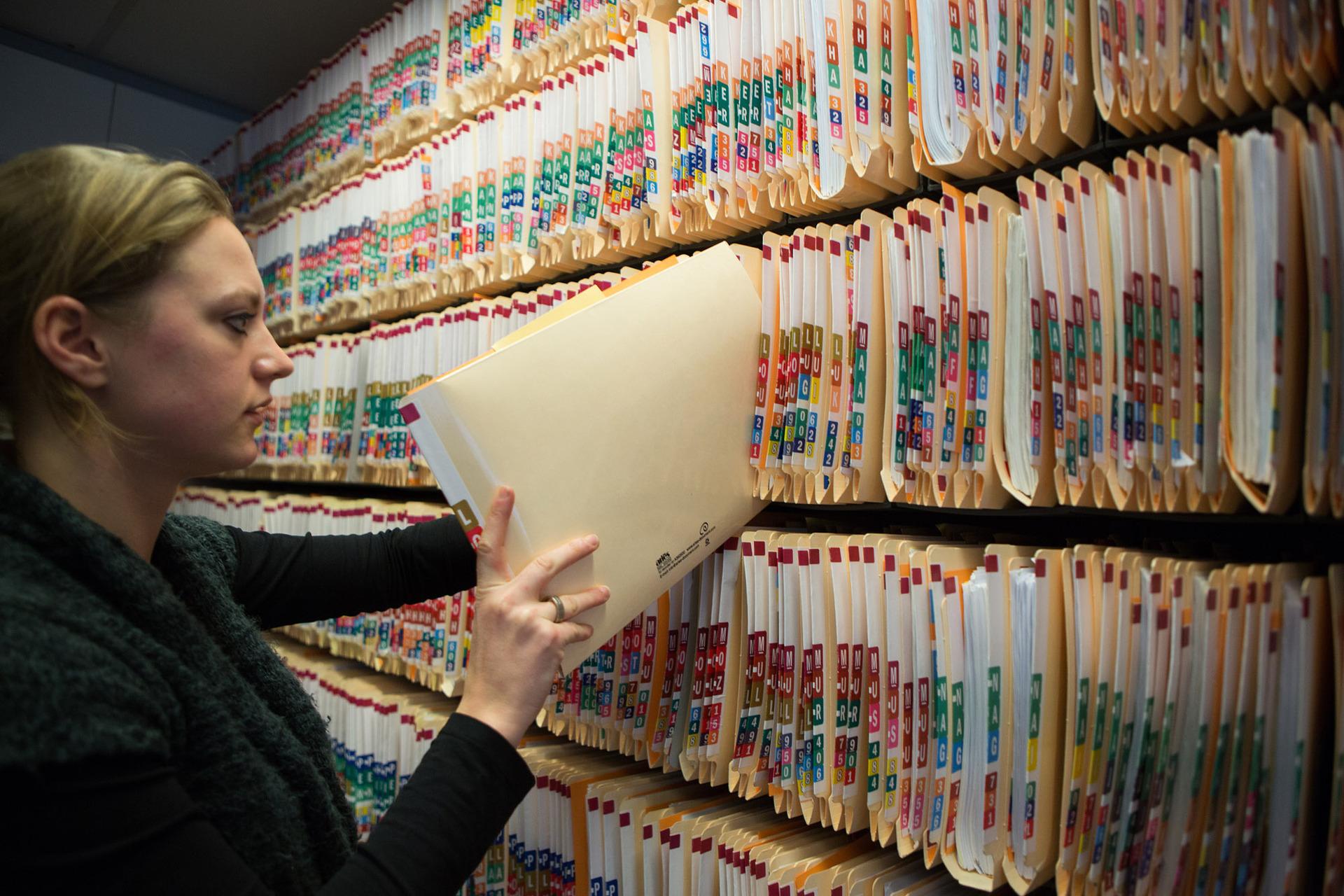 Een vrouw stopt een dossiermap in een archiefkast met mappen